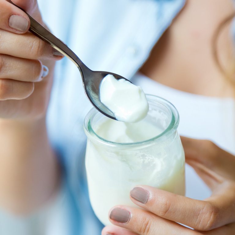 Eine Person hält einen Löffel mit Joghurt über einem Glas.